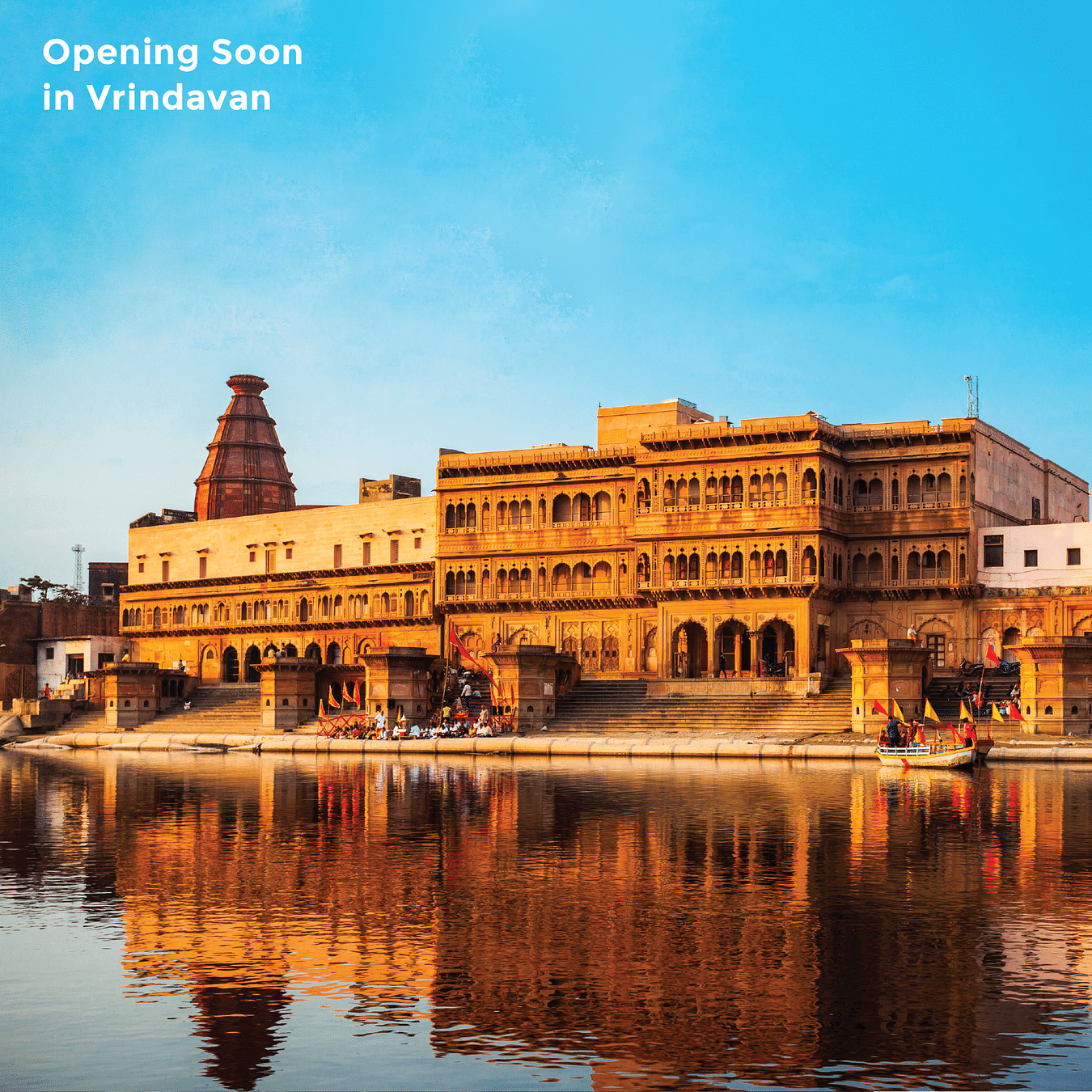 The Keshi Ghat in Vrindavan, India, is reflected in the Yamuna River at sunset, with ornate buildings and people gathered on the steps and text - Opening Soon in Vrindavan.