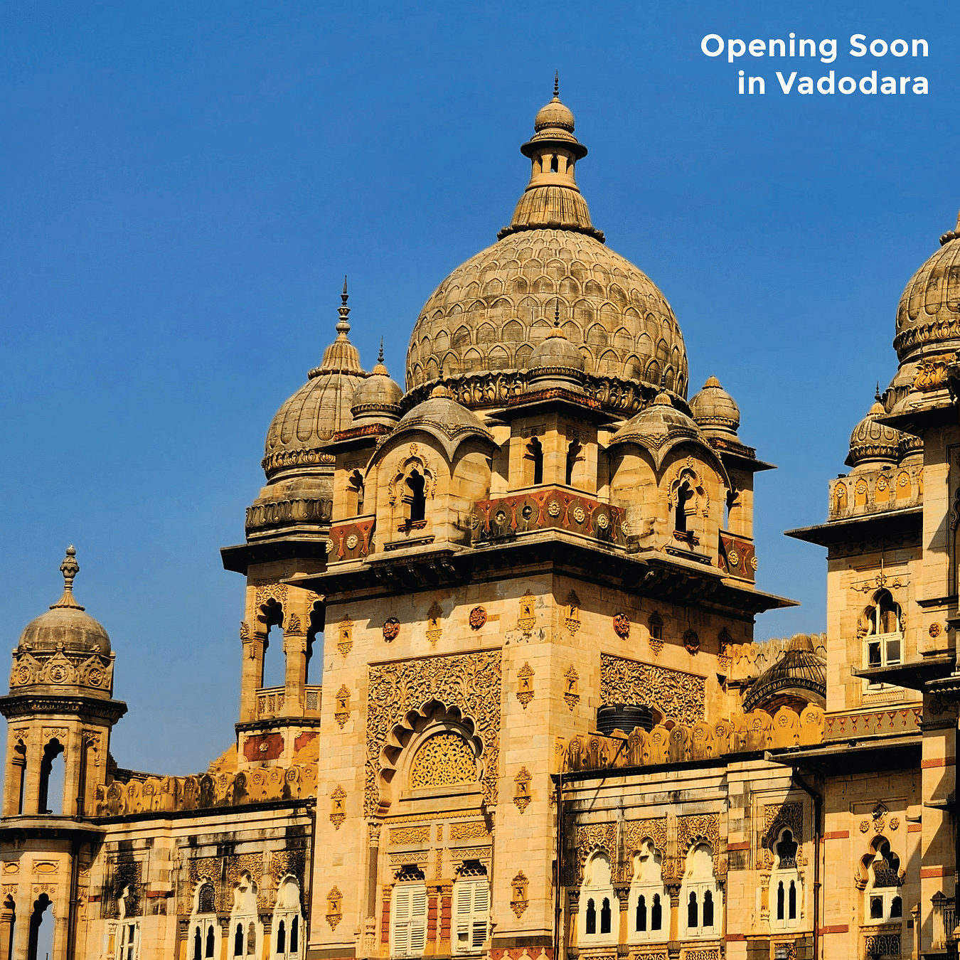 A detailed view of the ornate architecture of an Indian palace under a clear blue sky with text - Opening Soon in Vadodara.
