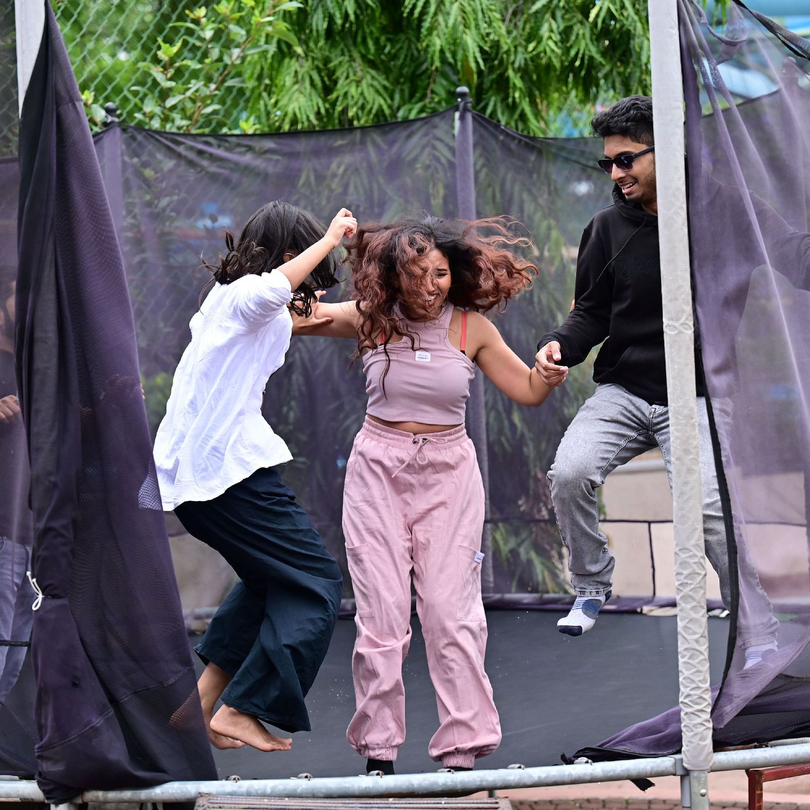 A close up shot of a group of people jumping on a trampoline with tree cover in the background.