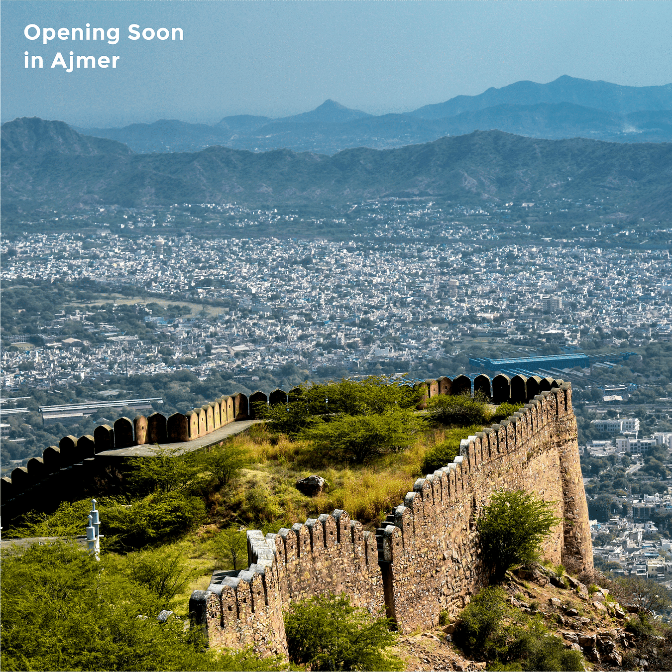 An image of the fort opening up to the landscape of Ajmer with the silhouettes of mountain in the backround as the text says 'Opening Soon in Ajmer'