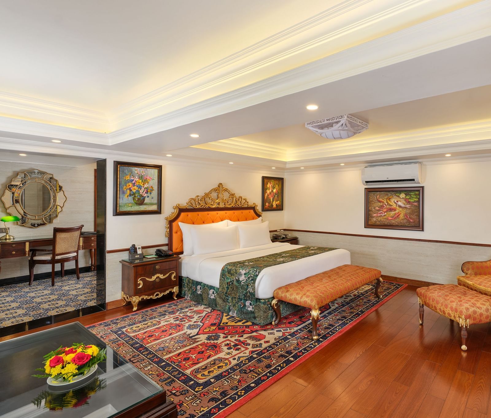 elegant Oriental Villa bedroom with a decorative rug beneath a grand bed, chair, table, TV and artworks on wall 
