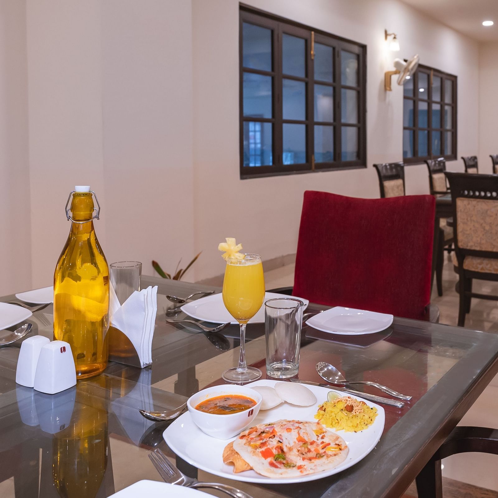 An indoor dining table set for a meal at Manorath Restaurant at Shri Vallabh Vilas Lords Plaza Nathdwara, with plated food, drinks , along with narrow dining table. 