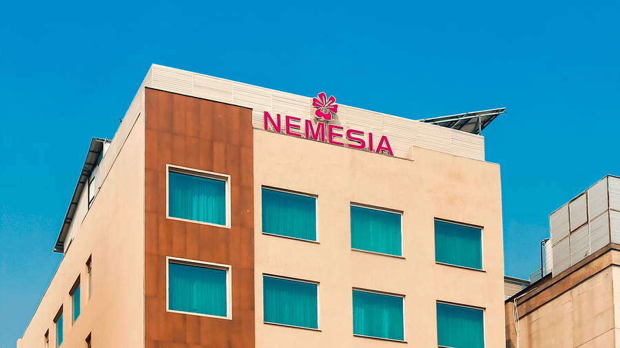 The facade of Nemesia City Centre in Gurgaon feauring the tall building coloured in beige and brown and some trees and bushes surrounding the property.