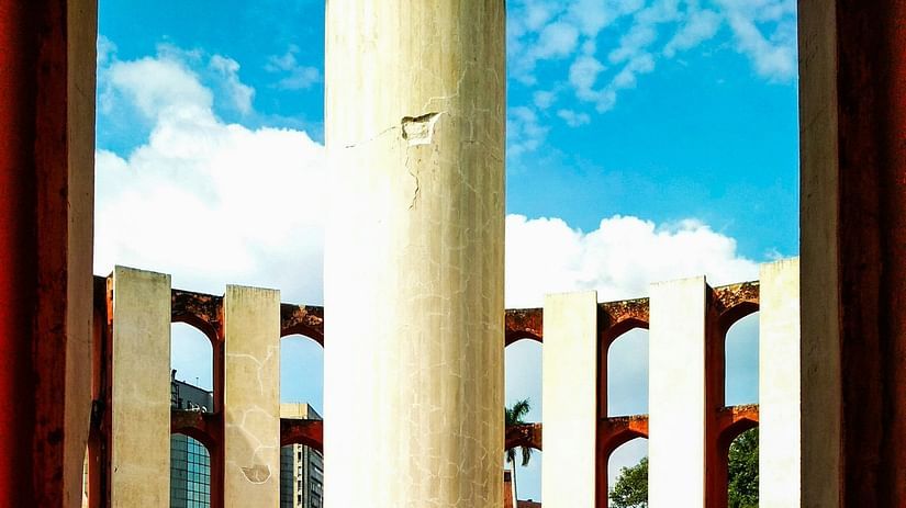 a pillar inside a structure with spaces in between and white clouds over blue sky in the background