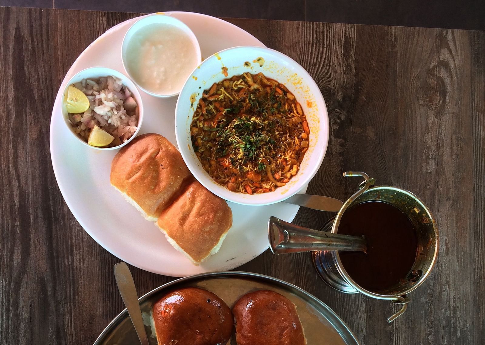 An aerial view of a breakfast spread that includes misal pav with onions, curd and other items.