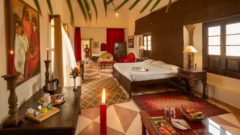 A richly decorated bedroom at Neemrana's Tijara Fort Palace includes a bed, seating area with red accents, artwork, and a tea/coffee setup.