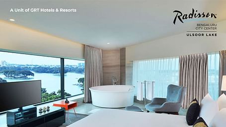 Modern lake-view suite at Radisson Bengaluru City Center featuring a plush bed, TV, and freestanding bathtub – part of the Bond and Beyond Summer Getaway offer.