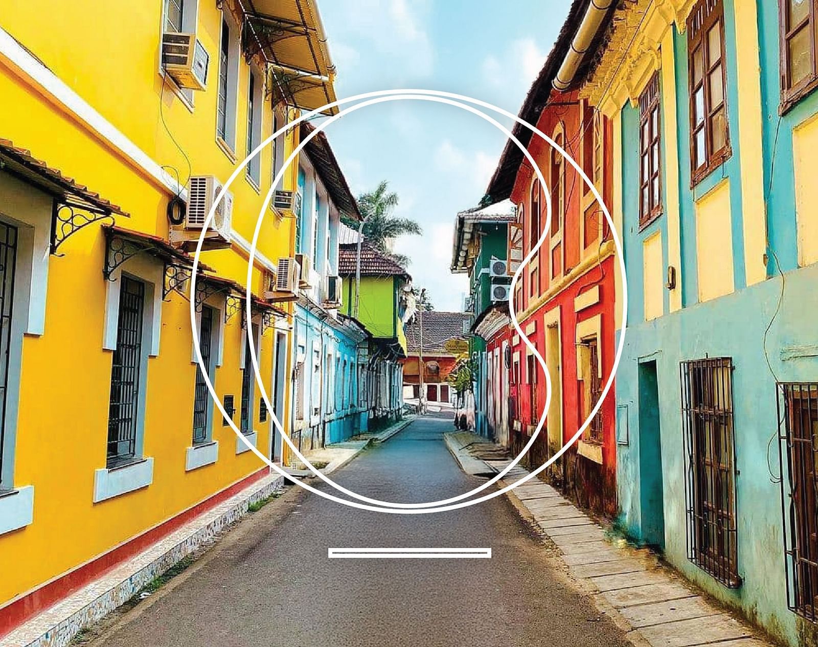 A wide angle shot of an alley in Goa with vibrant coloured buildings during a bright sunny day.
