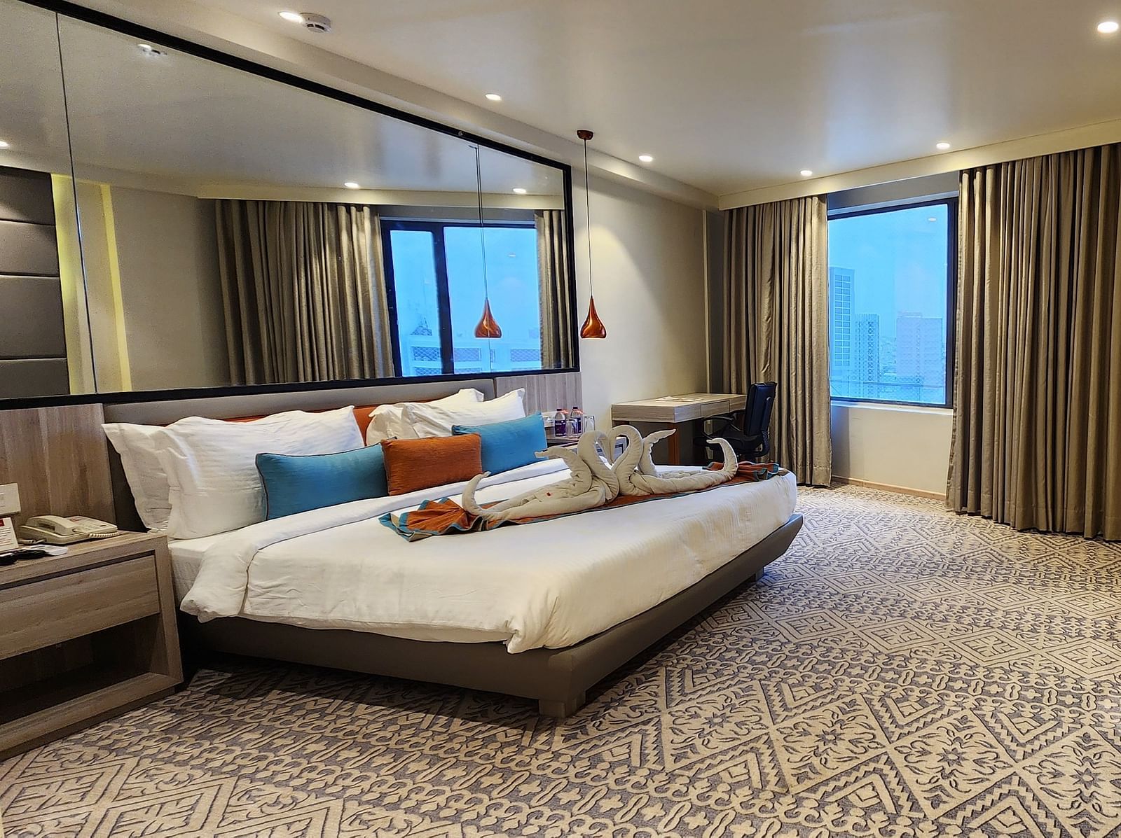 Spacious hotel suite with a modern double bed, mirrored wardrobe, and large window with curtains.