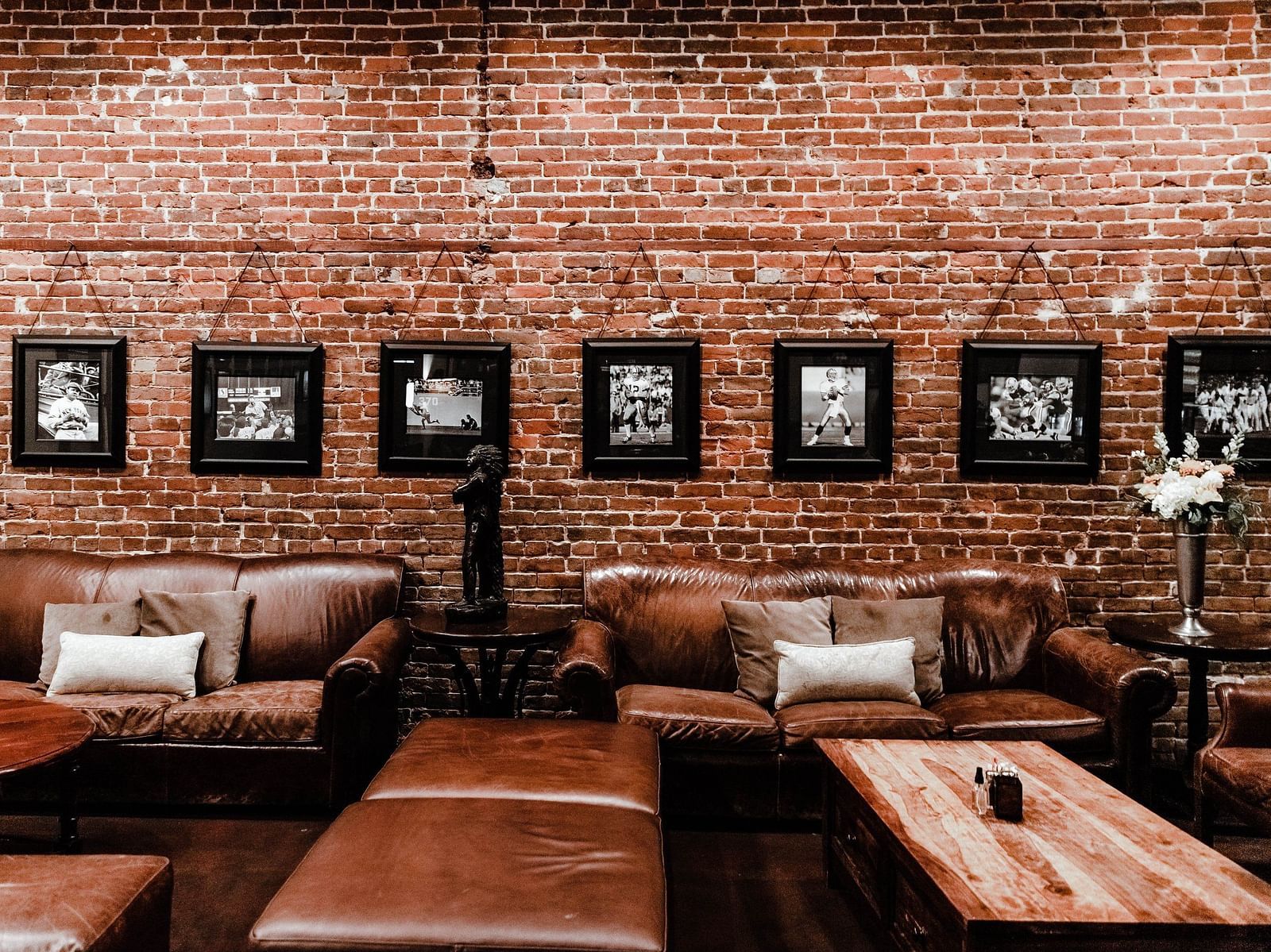 Sitting arena with brown sofas and wooden tables accompanied by brick textured wall with hanging wall art in the background 