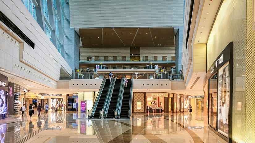 View of the inside of a mall where escalators, stores and people can be seen.