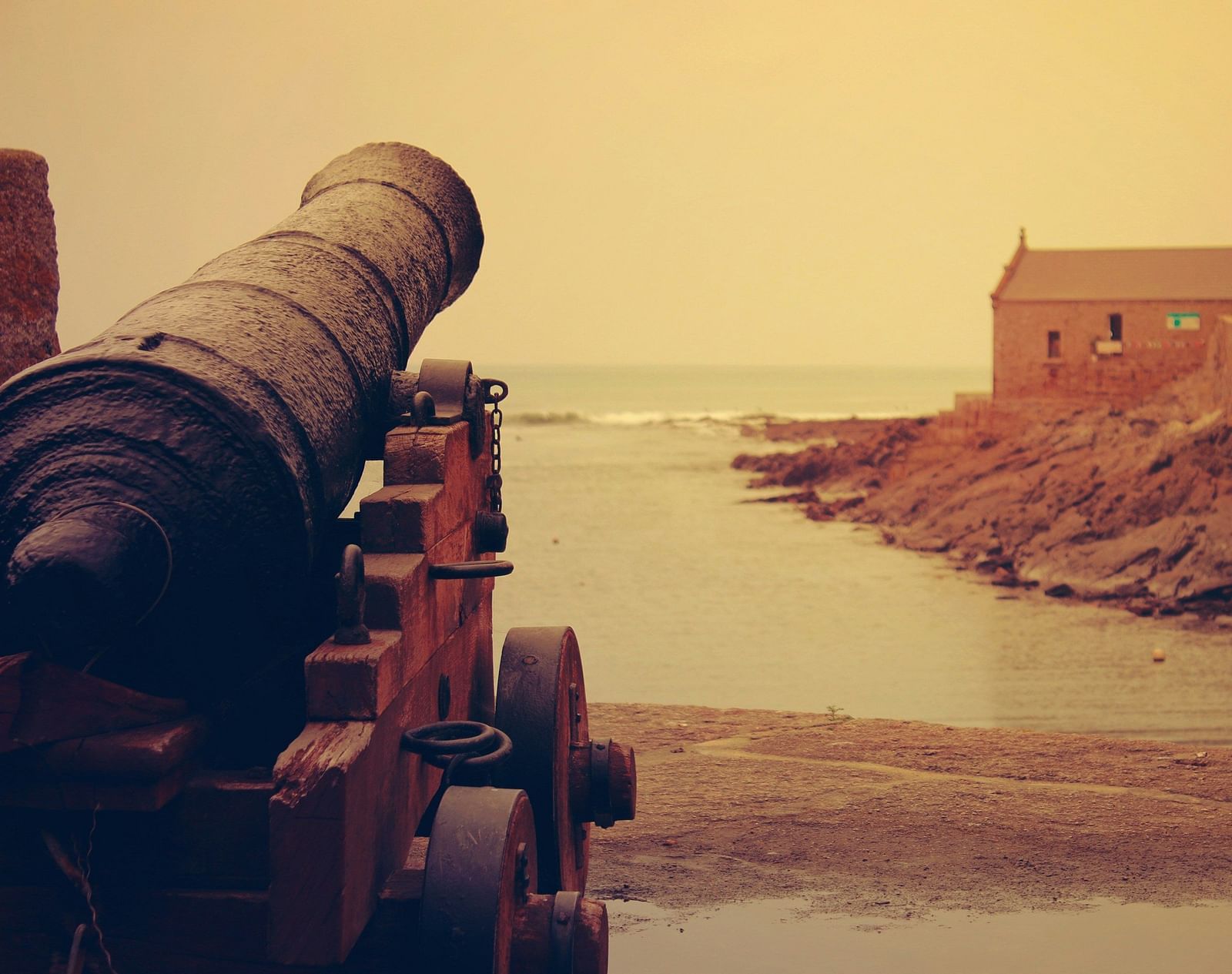 A cannon facing towards the ocean with a misty brown sky in the background.