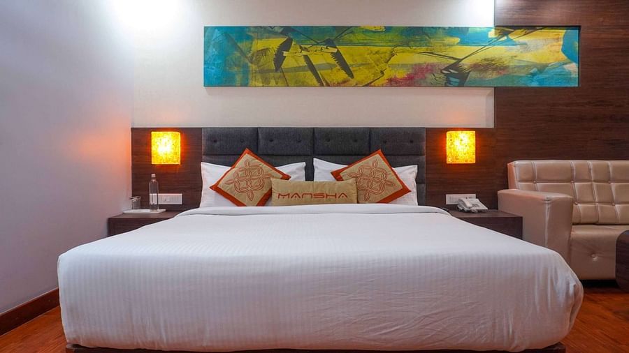 A room with a king size bed, bed side tables, lamps, and a sofa at Mansha Hotel Regency.