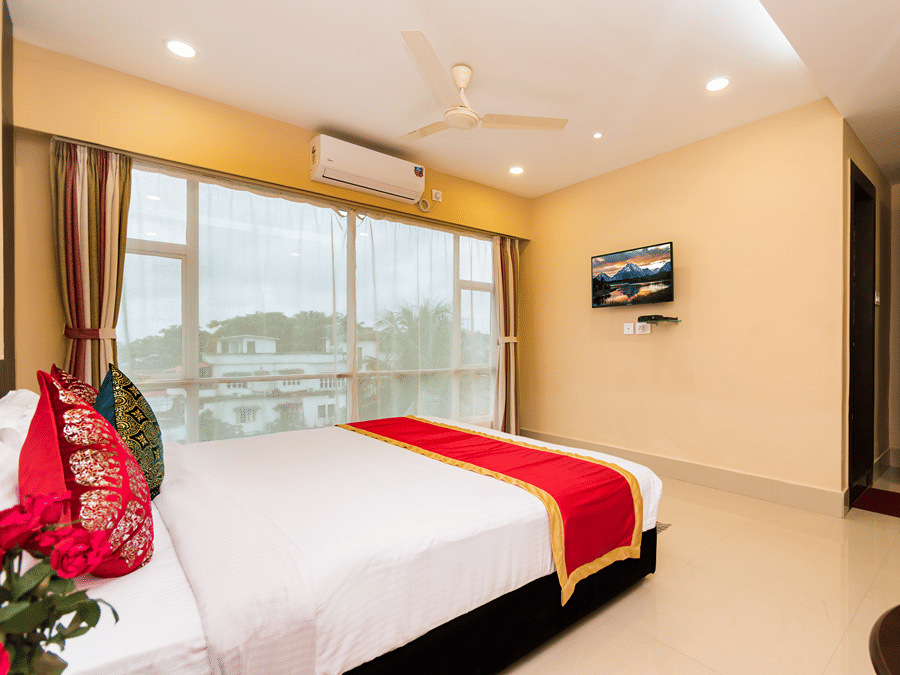 Bedroom at Central Courtyard Boutique Hotel, Siliguri, featuring a cosy bed with pillows, cushions, and bed runner facing a wall-mounted TV