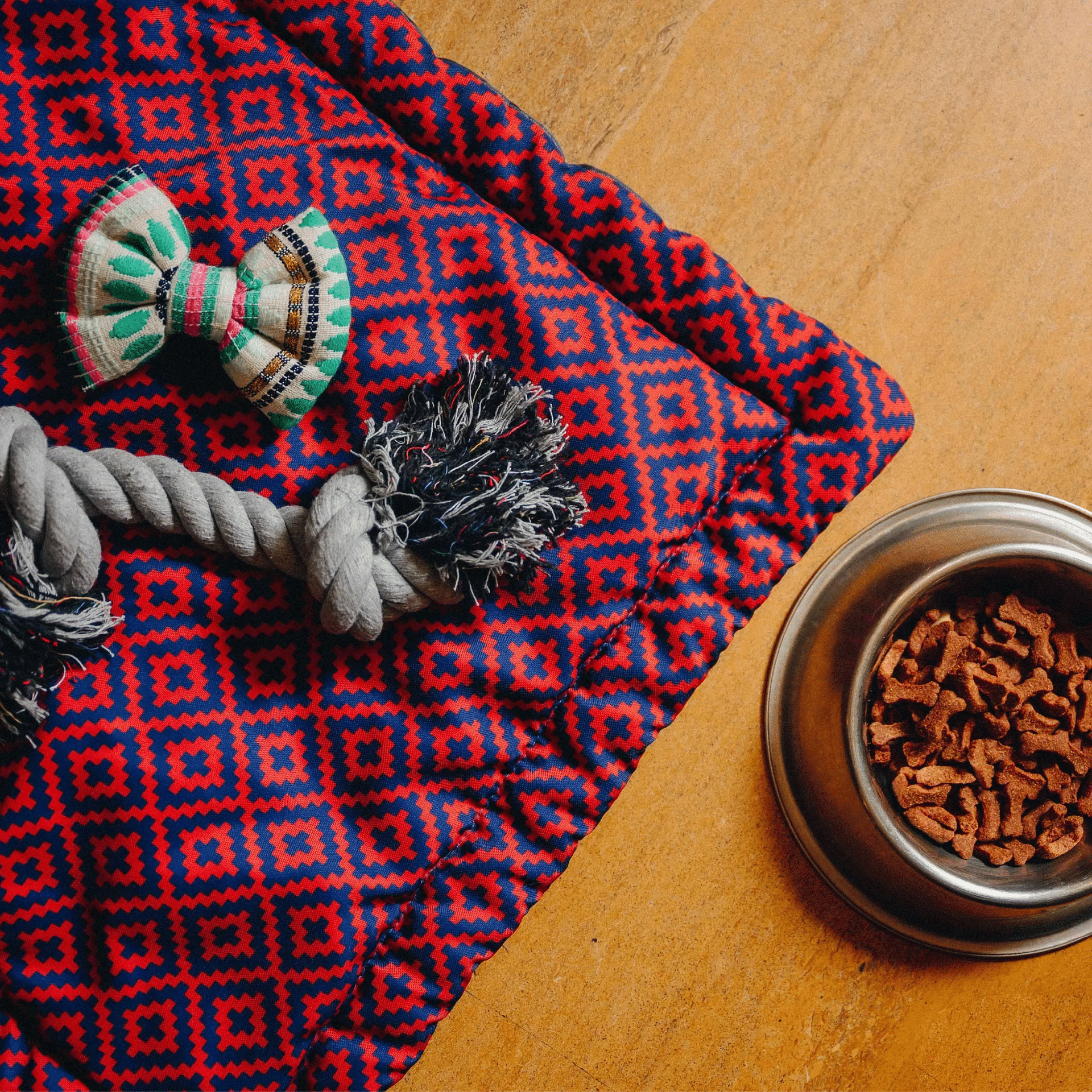 Floor setup at Karma Chalets with red patterned cloth, some pet toys, and a bowl of snacks for pets.