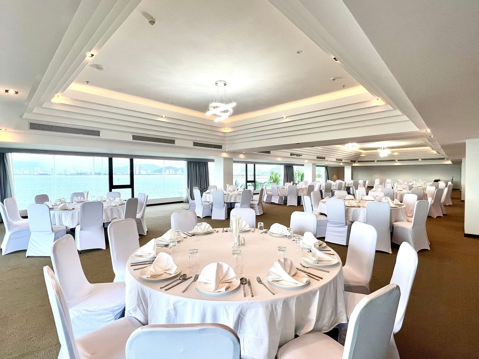 A round table seating arrangement in the Panorama hall with scenic view of the bay on the side - Alibu Resort
