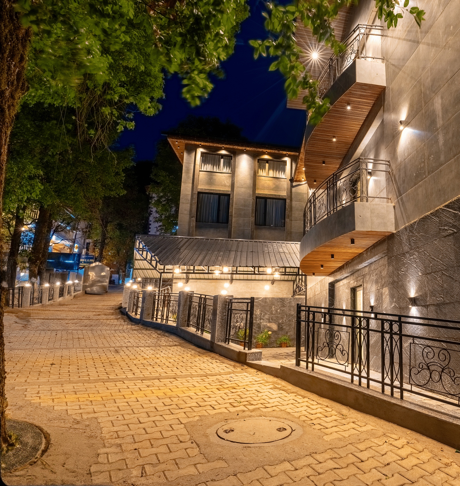 A well lit facade image of Bedzzz Xclusiv Ikshana Luxe at night which is surrounded by trees