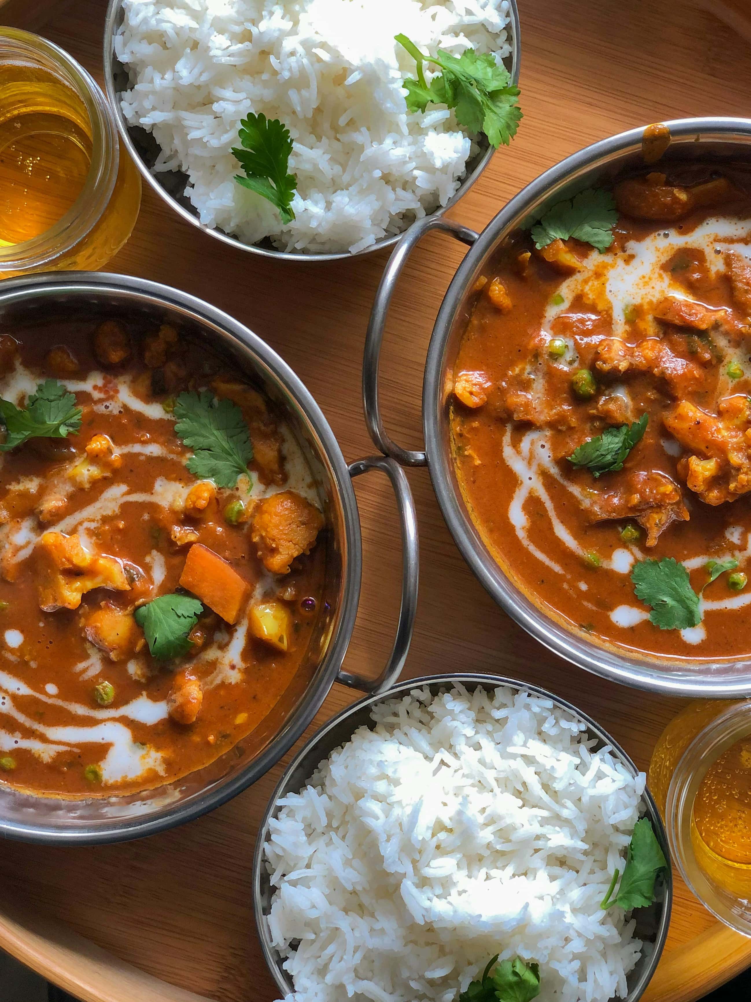 Vegetable curries in steel bowls with steamed rice and fresh coriander