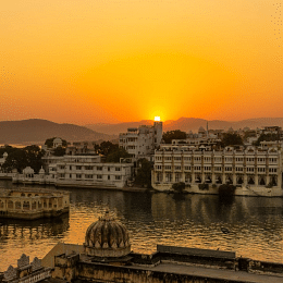 A sunset over Udaipur, Rajasthan, with buildings and Lake Pichola visible. 