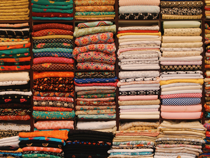 Neatly stacked piles of colourful, patterned fabrics on shelves in a textile shop, with a lone red chair in front.