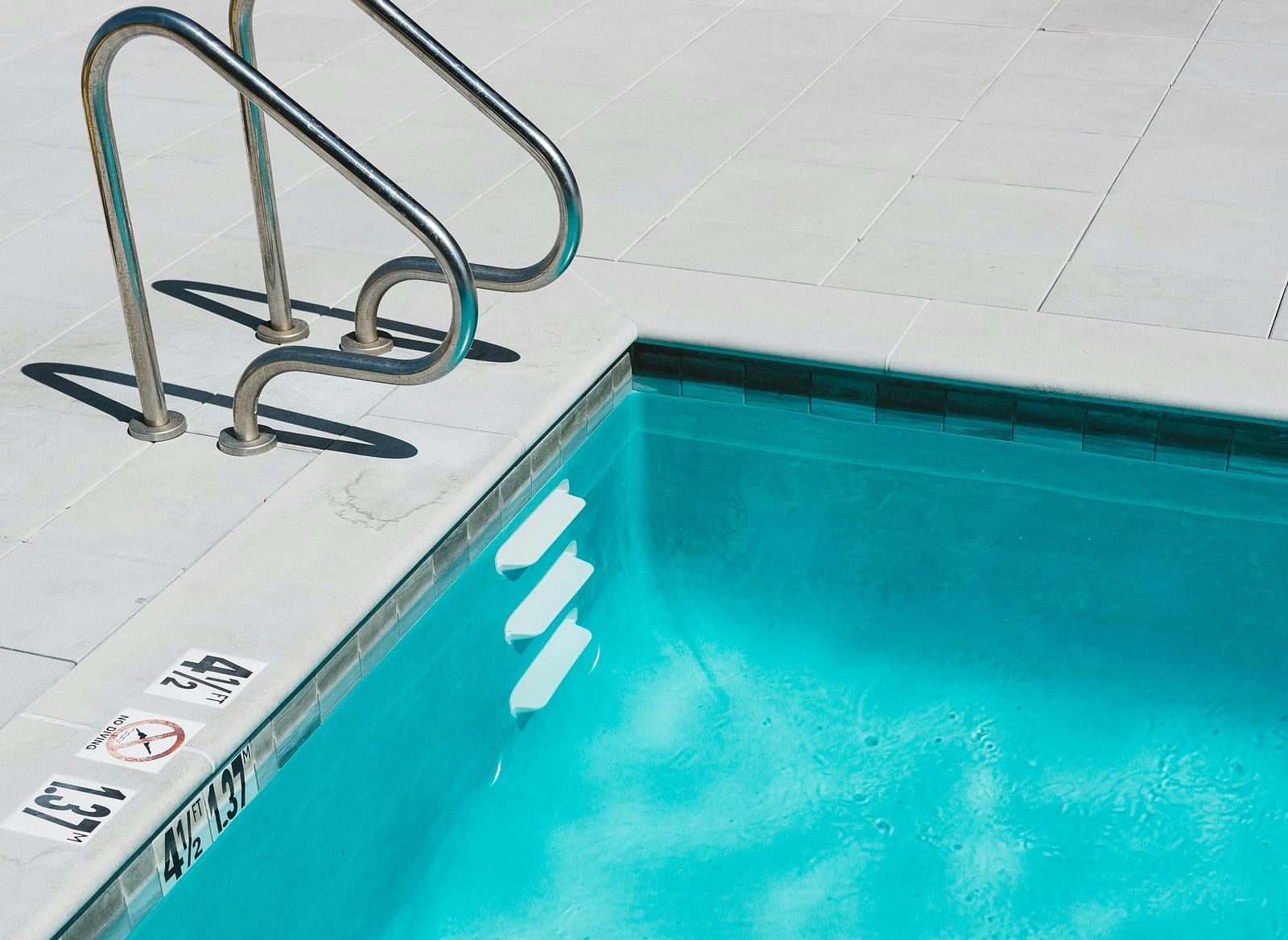 A swimming pool with clear blue water, a metal ladder, and a white pool deck.