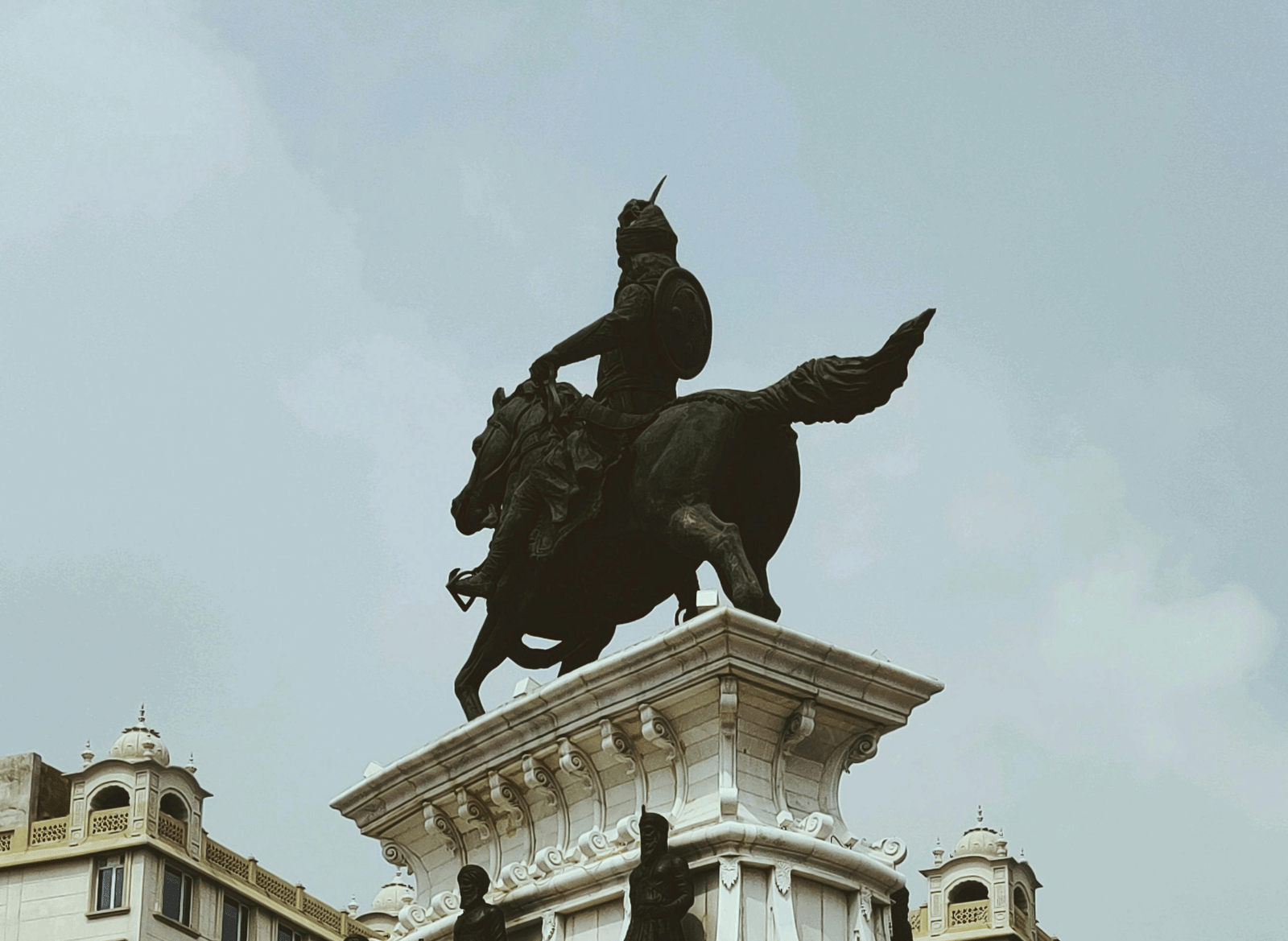 A large, white stone equestrian statue of a man on a horse, set on a multi-tiered pedestal under an overcast sky