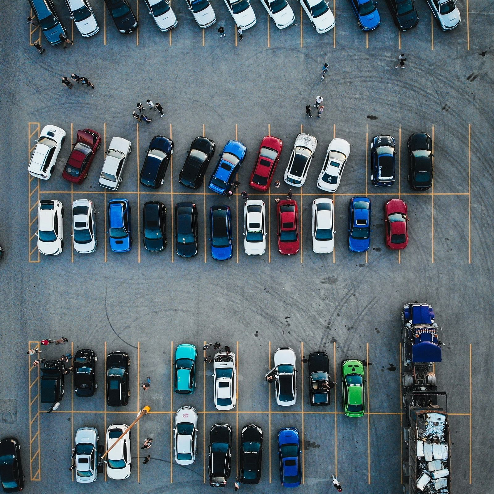 An aerial view of a crowded parking lot with a diverse assortment of parked cars and a few people walking between them