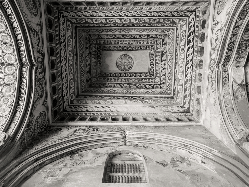 Monochrome architectural shot looking directly up at an intricately carved stone vaulted ceiling.