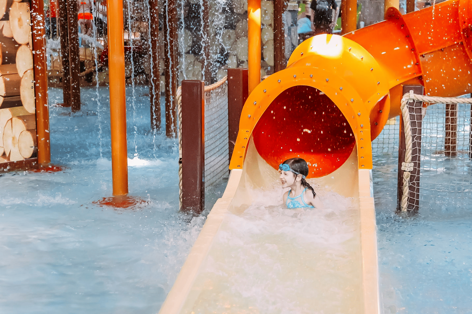 A kid is sliding down a bright orange water park slide into a pool of water.