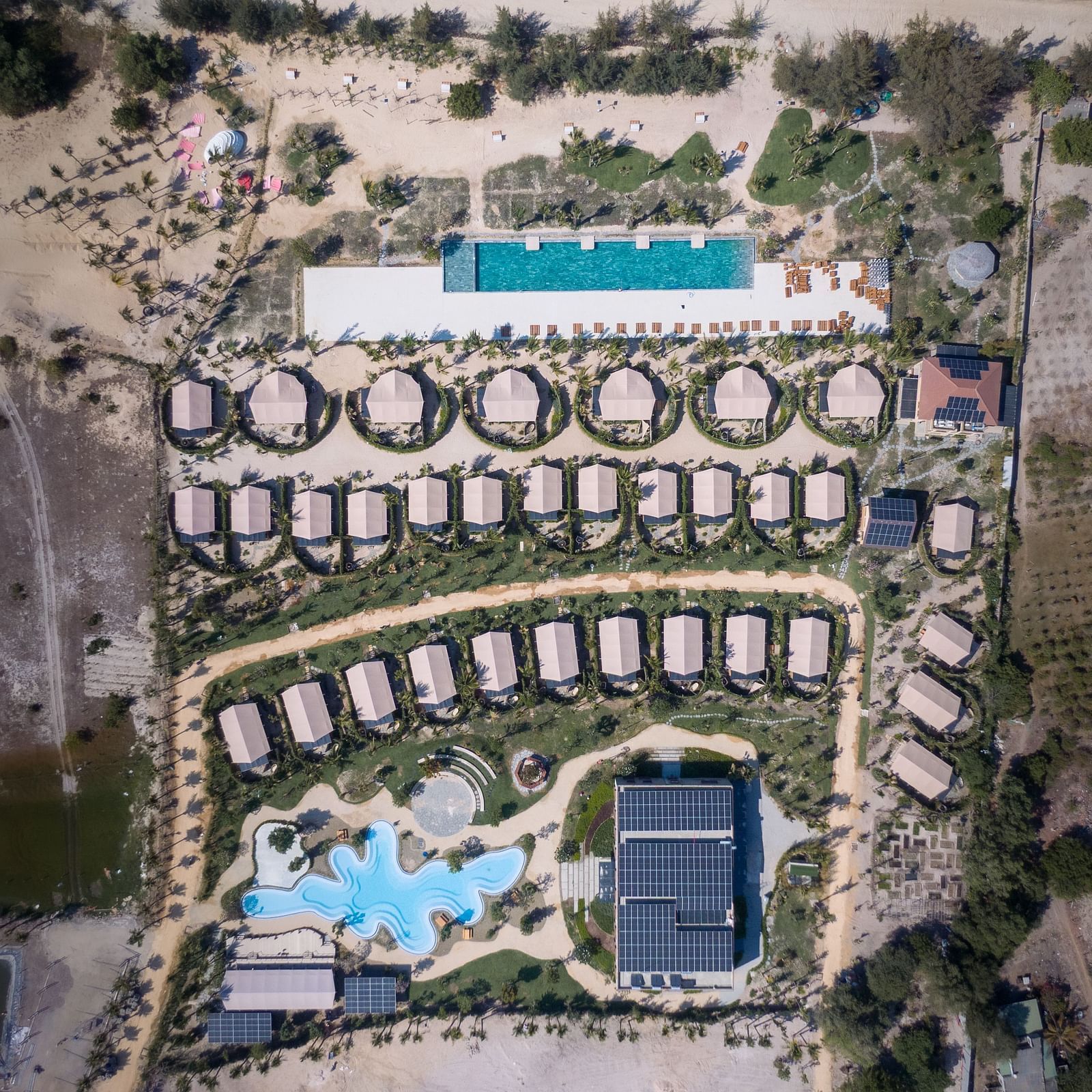 WoCAL Retreat Ke Ga featuring numerous circular bungalows, multiple swimming pools, and manicured green spaces nestled in a dry, coastal landscape.