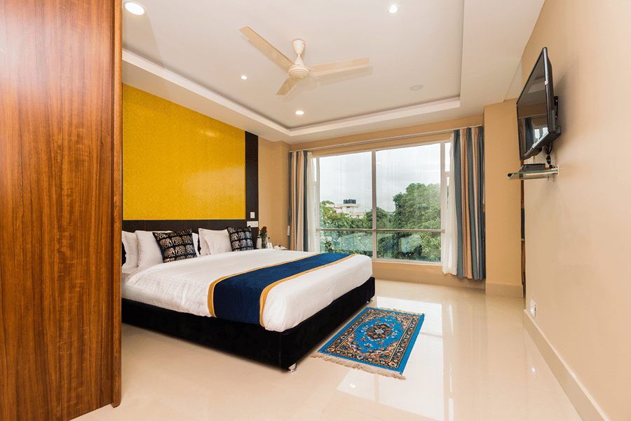 Bedroom of the Suite at Central Courtyard Boutique Hotel, Siliguri, featuring a plush bed by the ceiling-to-floor window facing the TV
