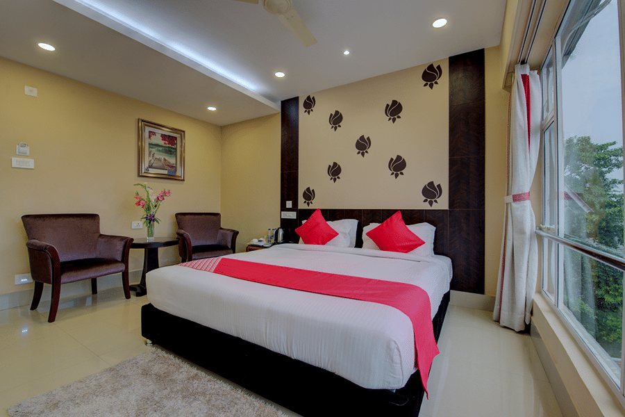 Super Deluxe Room at Central Courtyard Boutique Hotel, Siliguri, with a bed by a large window and a sitting area in the background