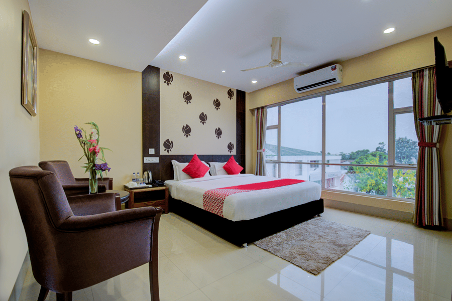 Super Deluxe Room featuring a plush bed by a window with an AC overhead opposite to the sitting space at Central Courtyard Boutique Hotel, Siliguri