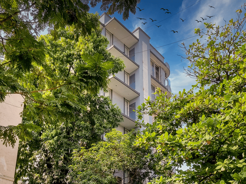 An exterior facade of Home2 Suites & Service Apartments, Mumbai Airport, with trees in the foreground.