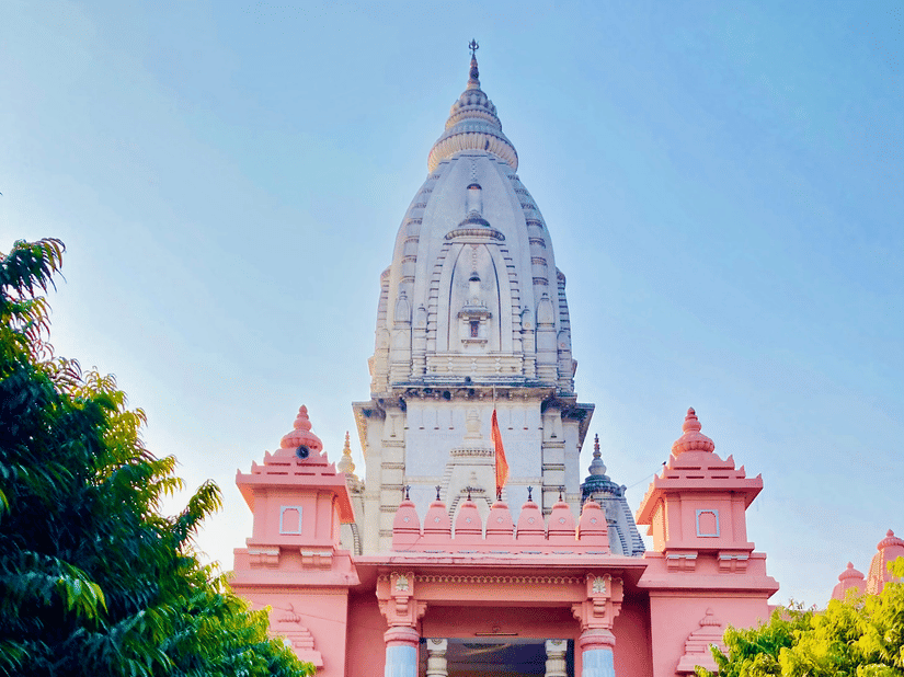 a white and pink temple in the distance with the pathway next to trees and blue sky in the background.