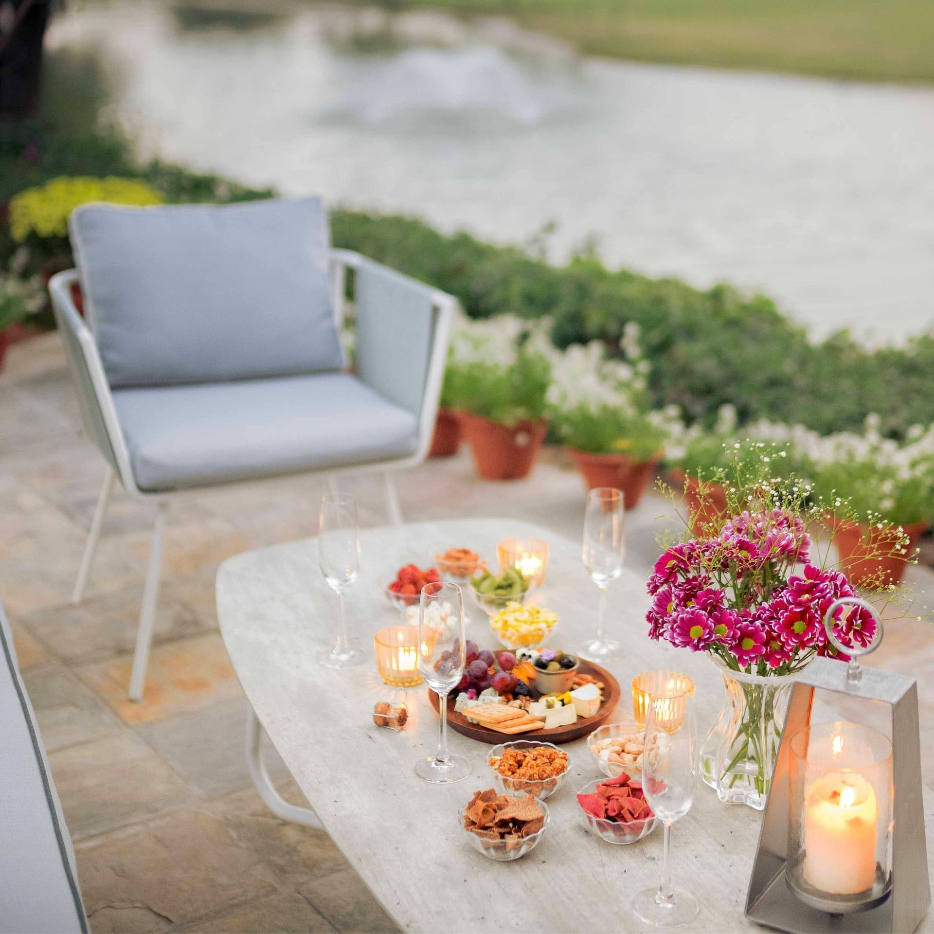Picturesque table with a romantic setup that includes candles, flowers, wine glasses and plates of food placed on a dock beside a running stream of water - Karma Chalets