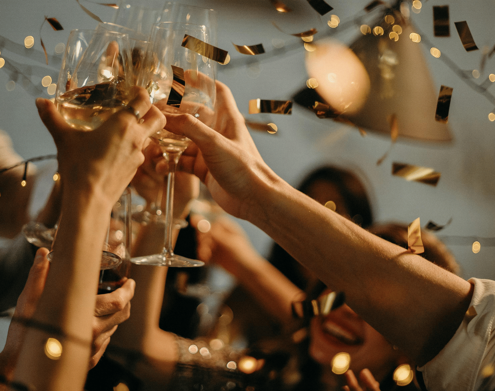 People making a toast with champagne glasses during a celebration, with gold confetti raining down.