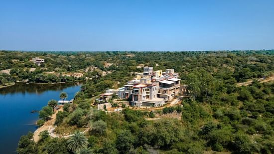 A palace amidst many trees on a small hill with a lake running next to it - Chunda Hotels