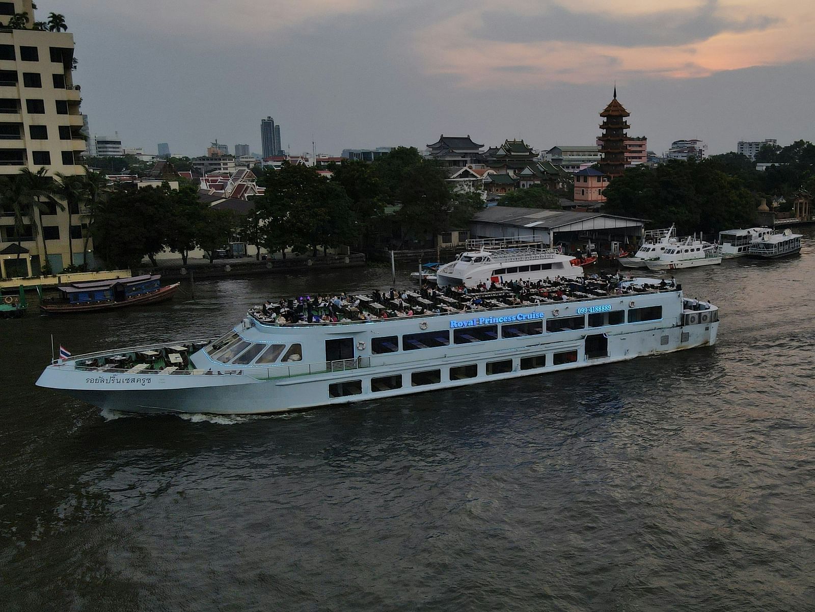 A boat carrying many people on the river with land in the background