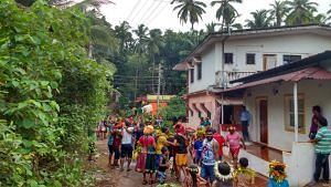 A group of people are gathered on a path between lush green trees and houses.