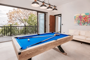 A spacious room boasts a billiards table and large sliding doors opening to a balcony with an expansive view.