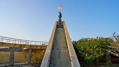 image featuring a statue holding an orange flag towards which the steps are leading to at the top at dev shree, deogarh