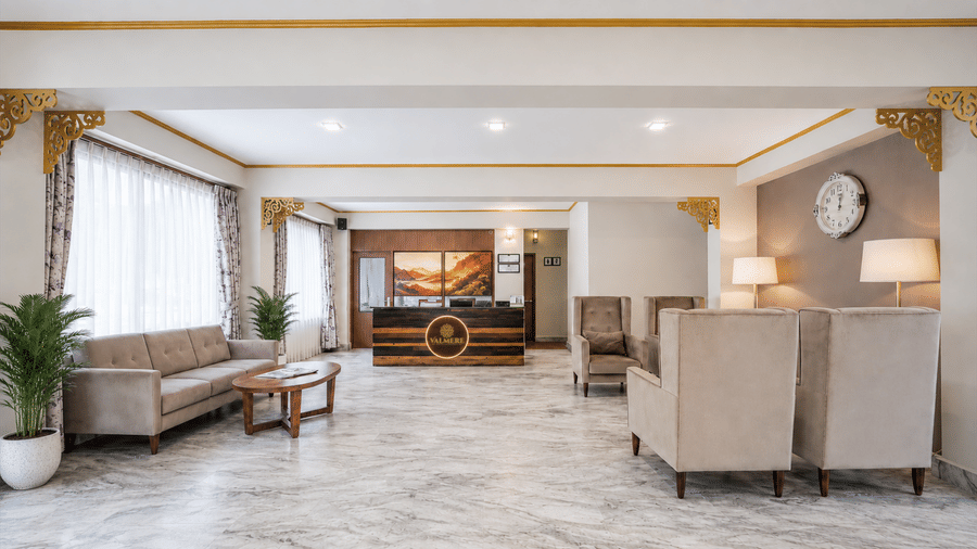 Lobby at Valmere Himalayan Hotel & Spa, Gangtok with a wood-panelled branded reception desk, marble flooring, beige sofas and armchairs, and a round wall clock.