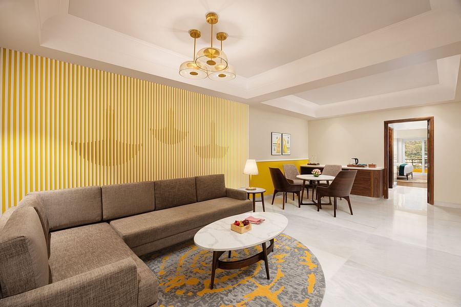 A chic living room with a grey sectional, a white coffee table on a patterned rug, a yellow striped wall, a dining set, and an open doorway to a bedroom - Aloha On the Ganges.