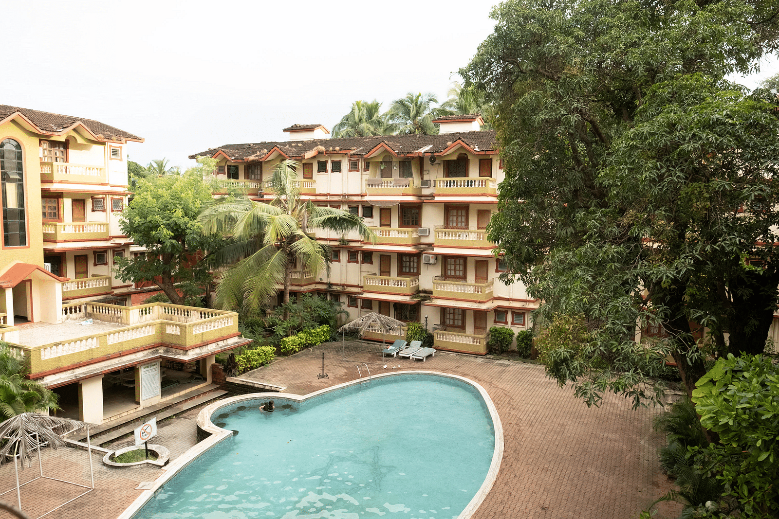 Facade of  Vistar Holidays, Goa with a swimming pool in front and trees besides it.