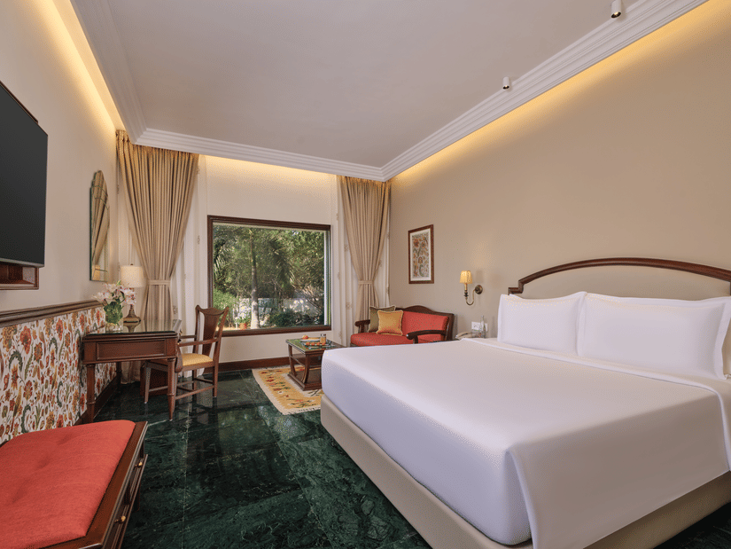 The Premium King Garden View Room at The Ummed Ahmedabad featuring a spacious interior with warm lighting and a king size bed facing the TV mounted on the wall