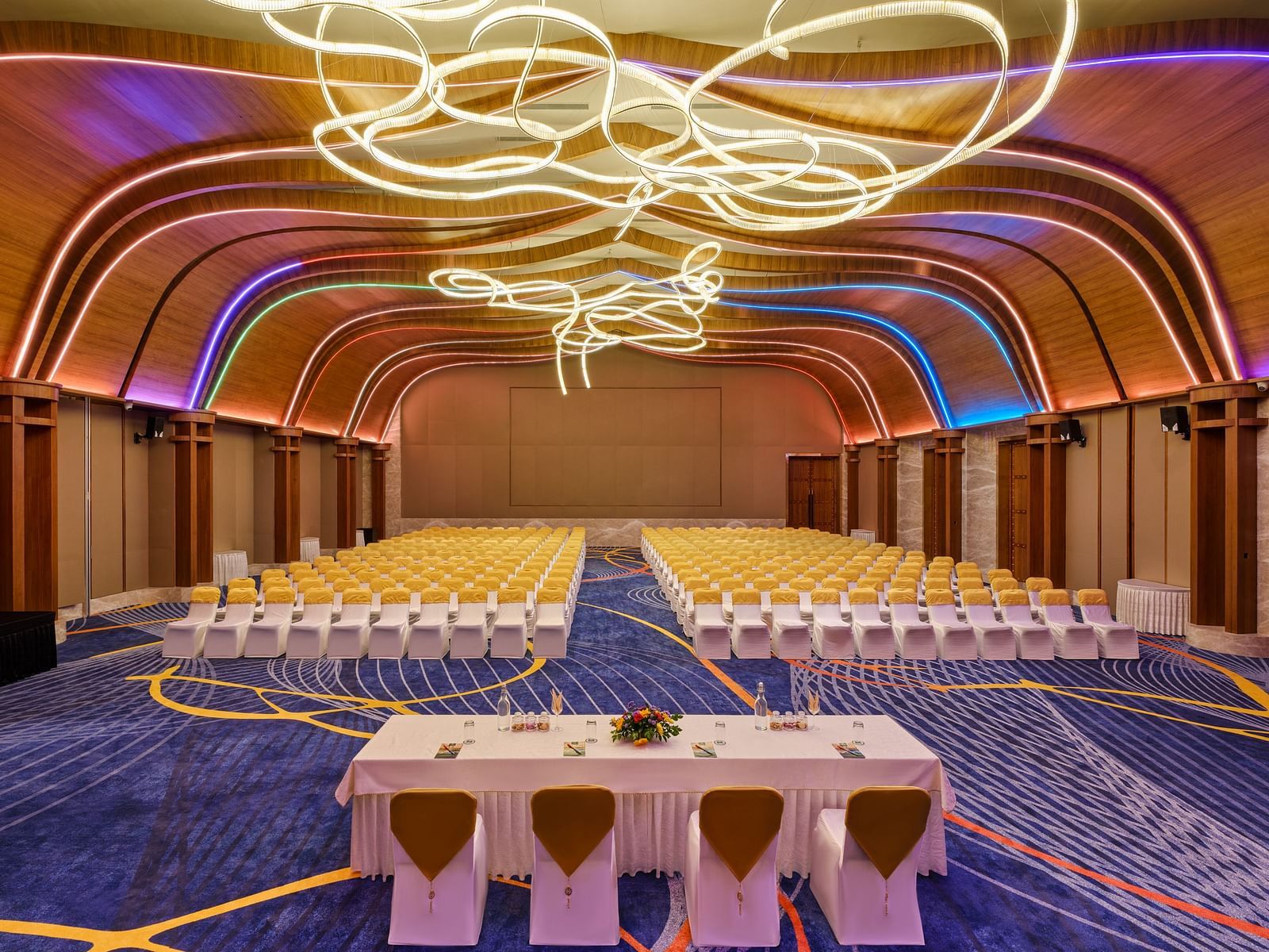 Image of the meeting hall Boito Voyage at Swosti Premium Beach Resorts in Puri featuring a large sitting area for audience under warm lighting and four chairs arranged with a large table facing the audience