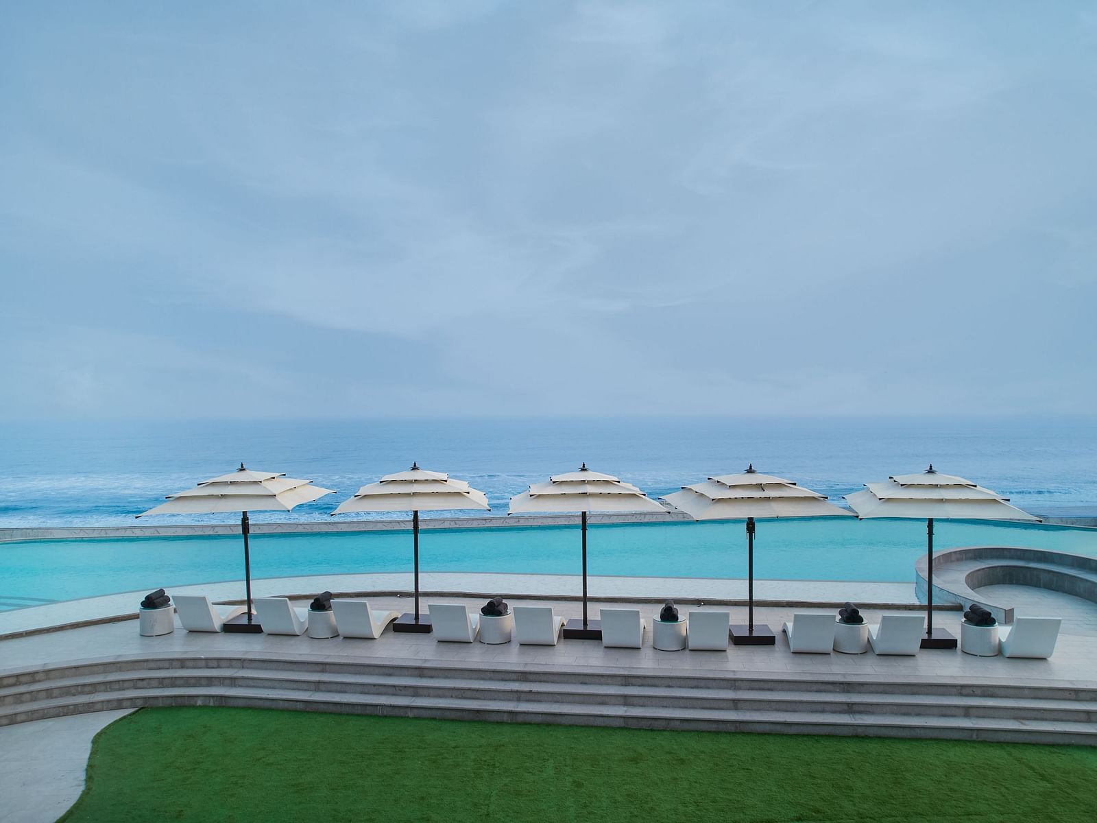Swimming Pool at Swosti Premium Beach Resorts in Puri under a cloudy sky featuring pool deck and an infinite view of the sea appearing to be almost blended with the sky