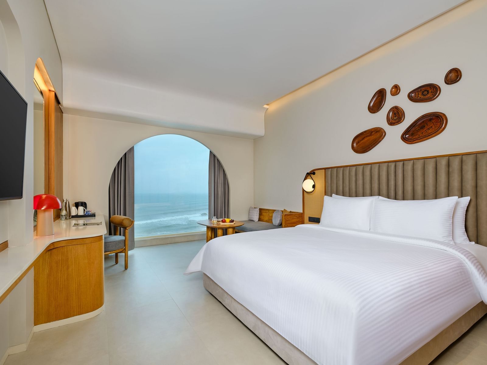 Image of the Sea View Room at Swosti Premium Beach Resorts in Puri featuring a plush bed and a TV next to which a work desk is placed beside the huge window with sea view