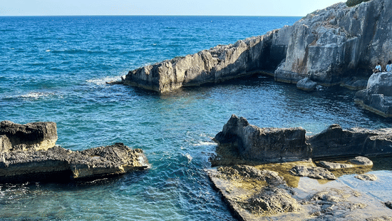 View of Talpe Natural Pool near Galle Sri Lanka with rocky outcrops, clear turquoise water, and a bright blue sky in the background.